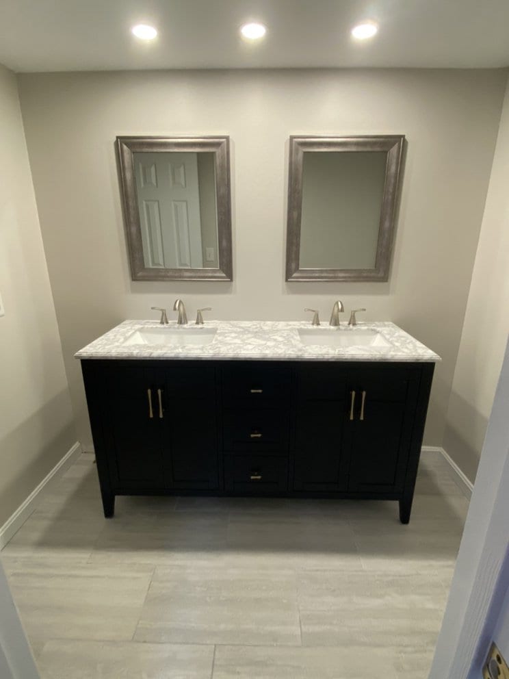 Finished bathroom with a dark double vanity, marble-effect top, two framed mirrors and recessed ceiling lights.