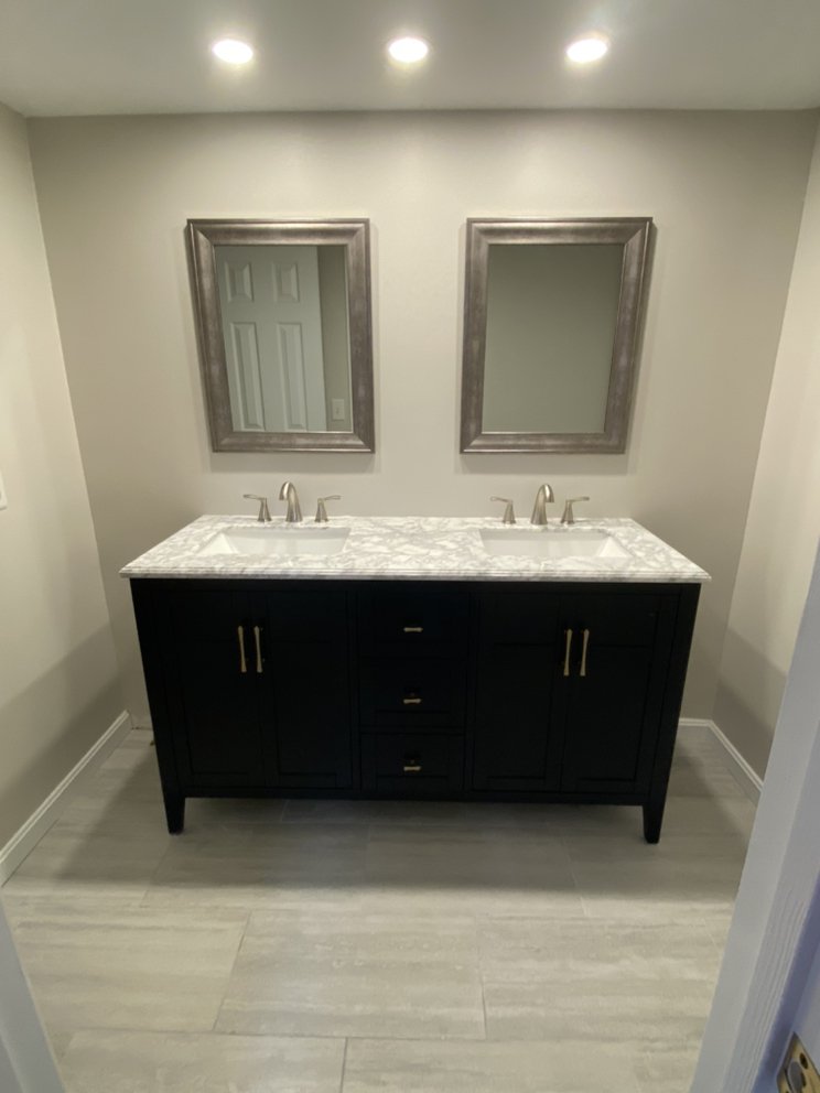 Finished bathroom with a dark double vanity, marble-effect top, two framed mirrors and recessed ceiling lights.